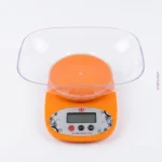 Orange digital kitchen weighing scale featuring LCD display, tare function, and detachable measuring bowl.